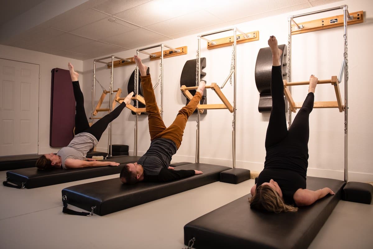 Three clients on mats in shoulder bridge with legs to the Tower push-through bars
