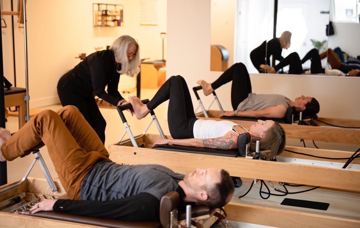 A teacher adjusting a client's foot on the Reformer footbar during a class