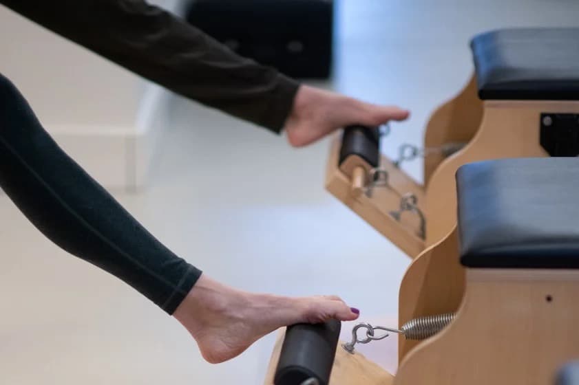 A hand and a bare foot on the Wunda Chair pedal, spring and hardware in focus