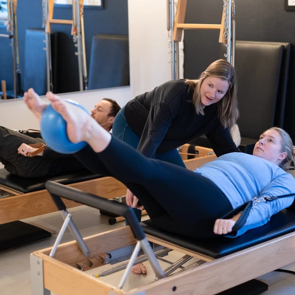 A teacher coaching a client on the Reformer with a second client working behind