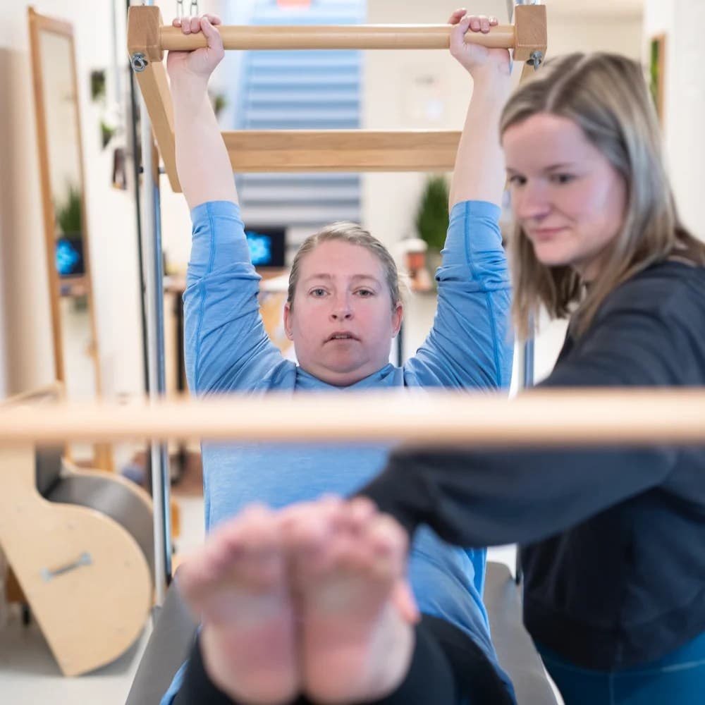 A client working on the Reformer roll-down bar with a teacher watching closely